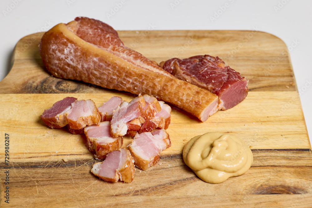 Ham cut into pieces and mustard on a wooden plate. Ham cut into pieces and mustard on a wooden plate.