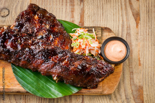 Billede på lærred Close up of BBQ spare ribs with coleslaw and sauce on wooden table
