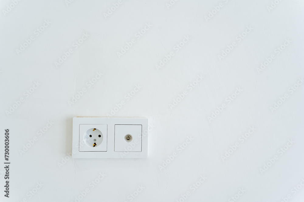 A rectangular white wall socket with a power plug and socket for electrical supply. A rectangular white wall socket with a power plug and socket for electrical supply.