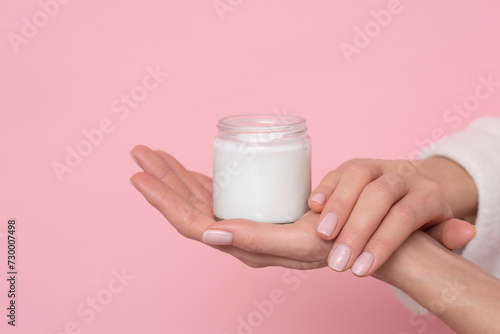Female hands with cream on pink background.