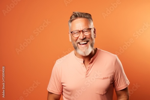 Portrait of happy senior man in glasses and polo shirt on orange background.