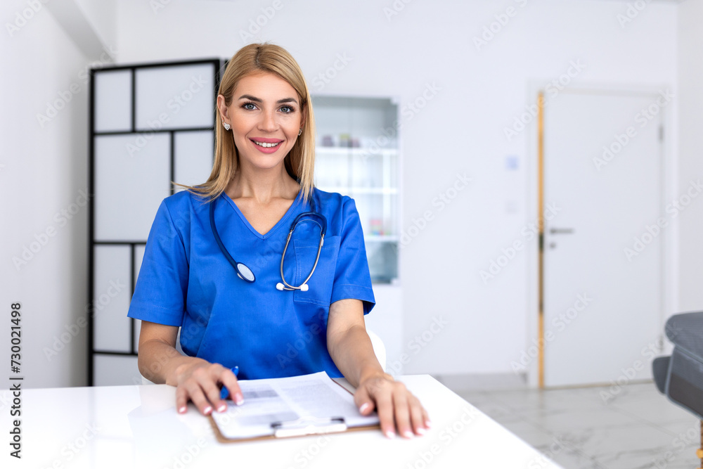 Portrait of young female doctor sitting in clinic office, filling out medical form at table. Portrait of young female doctor sitting in clinic office, filling out medical form at table.