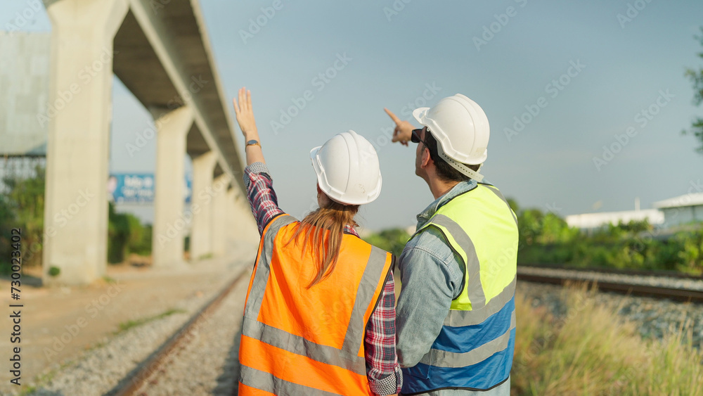 Back view of two engineers in safety uniform and helmet discussion and inspection construction process railway. Two engineer working on railway together. Teamwork concept Back view of two engineers in safety uniform and helmet discussion and inspection construction process railway. Two engineer working on railway together. Teamwork concept