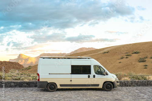 A white van is parked on the side of a road amidst natural surroundings.