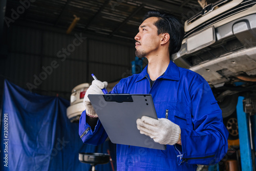 Asian Japanese mechanic male worker employee checking car in auto service workshop maintenance replace fix auto part checklist