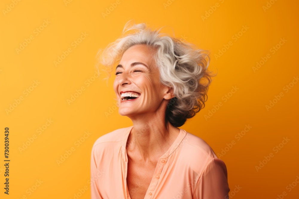 Happy senior woman with closed eyes laughing and looking up on yellow background