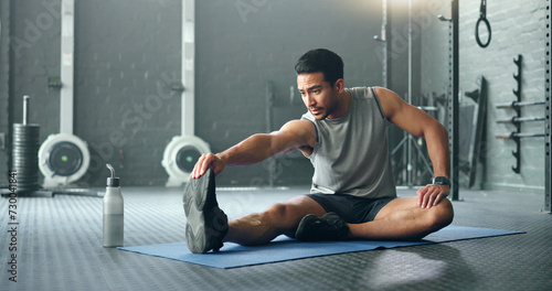 Man, break and stretching on gym floor in fitness, workout or training for strong muscles, heart health or cardio wellness. Japanese personal trainer, sports person or coach in body warmup exercise