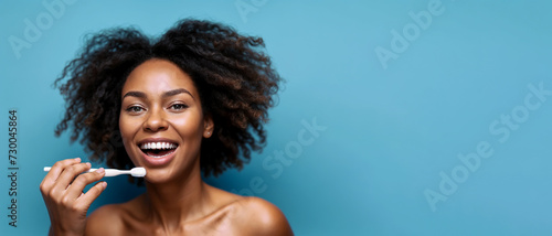 Beautiful young African woman with a beautiful smile, brushing her teeth with a toothbrush on a blue background. Banner. Copy space
