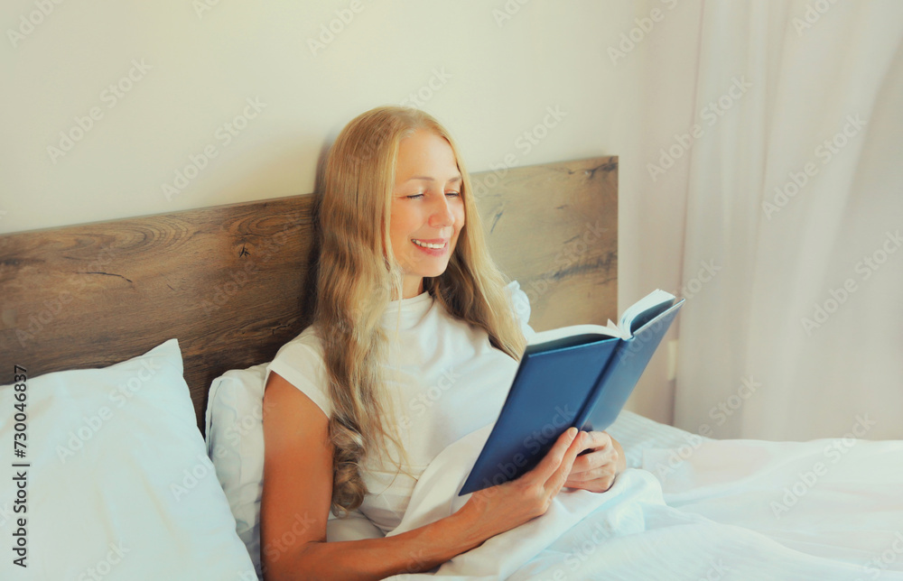 Happy middle aged woman reading book lying on the bed at home Happy middle aged woman reading book lying on the bed at home