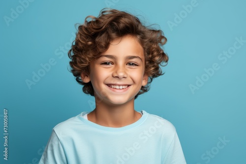 smiling little boy with curly hair looking at camera on blue background