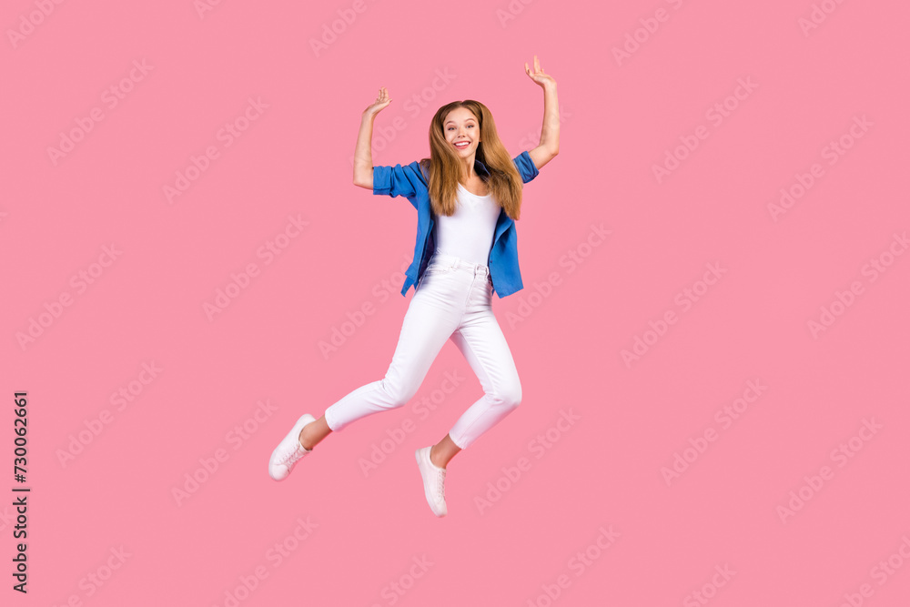 Full length photo of cute sweet girl wear blue shirt jumping high rising arms isolated pink color background Full length photo of cute sweet girl wear blue shirt jumping high rising arms isolated pink color background