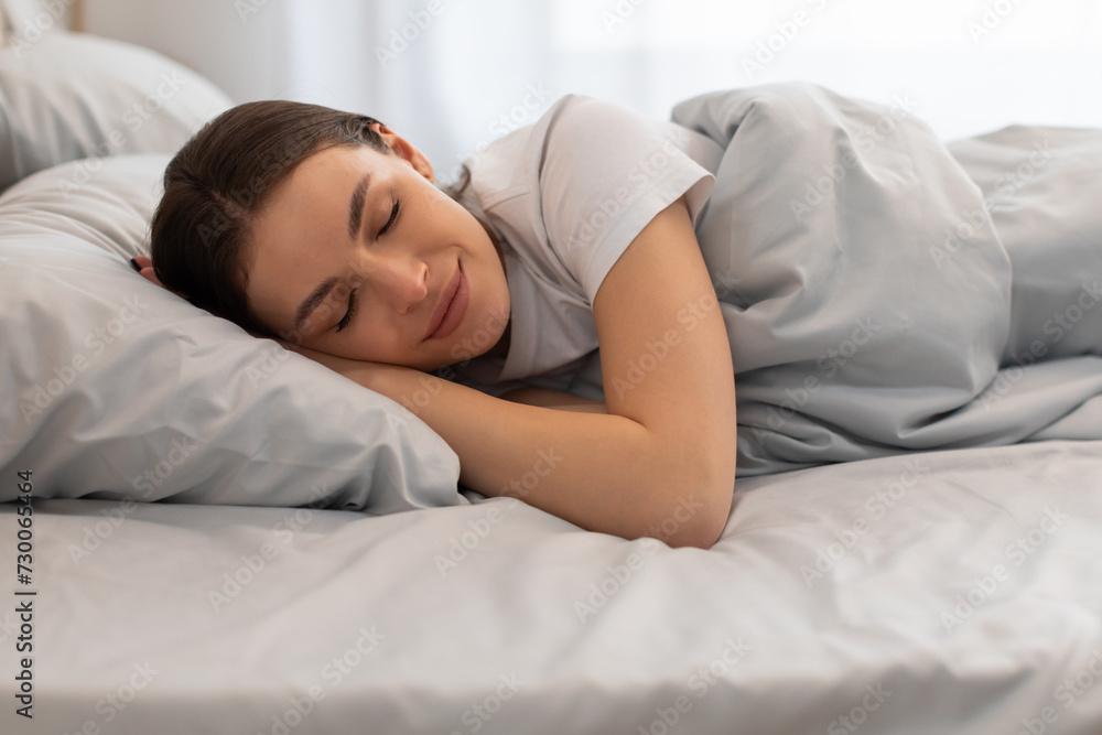 Serene young woman smiling while resting in bed Serene young woman smiling while resting in bed