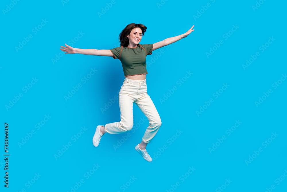 Full size photo of good mood carefree woman wear green t-shirt white trousers hold palms like wings isolated on blue color background