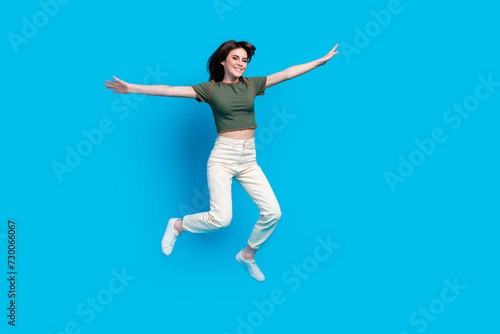 Full size photo of good mood carefree woman wear green t-shirt white trousers hold palms like wings isolated on blue color background