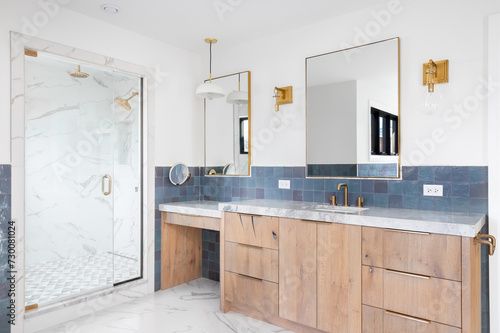 A luxurious bathroom with a wood vanity cabinet, blue tiles on the walls, gold accented lights and mirrors, and a large walk-in shower lined with marble tiles. No brands or labels. photo