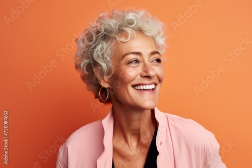 Portrait of happy senior woman smiling at camera over orange background.