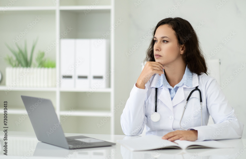 Pensive beautiful millennial woman doctor sitting at her office Pensive beautiful millennial woman doctor sitting at her office