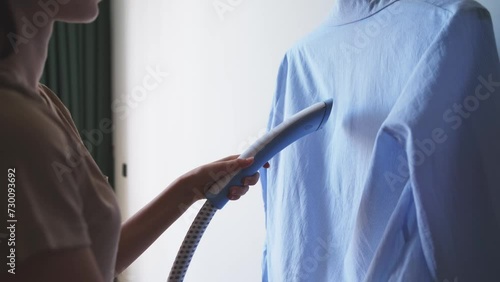 A woman steams a shirt with a hand iron and smooths out the creases on it. Housewife chores, tidying up, cleanliness, domestic lifestyle