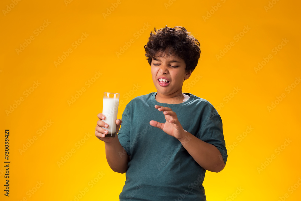Dairy intolerant unhappy child boy holding glass of milk over yellow background. Lactose intolerance. Dairy intolerant unhappy child boy holding glass of milk over yellow background. Lactose intolerance.