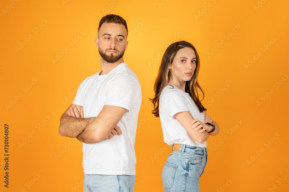 A man and woman in white shirts and denim jeans stand back to back with arms crossed A man and woman in white shirts and denim jeans stand back to back with arms crossed