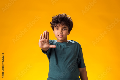 Child boy showing stop gesture on yellow background. Bulling and negative emotions concept