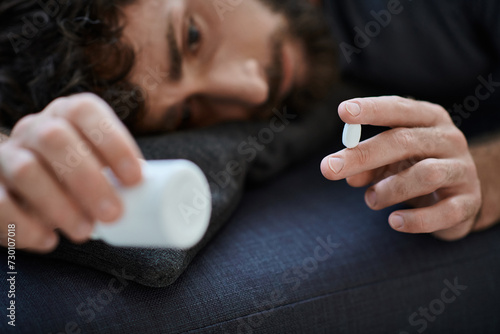 ill suffering man in casual attire lying on sofa with pills in hand  mental health awareness