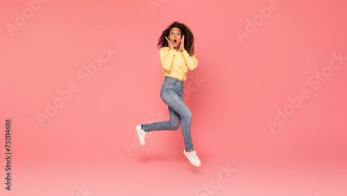 Surprised black woman jumps, touches cheeks, excited on pink backdrop