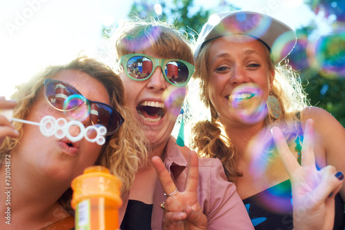 Women  friends and bubbles for blowing or happy outdoor with sunglasses or peace sign for holiday and relax. People  face and plastic wand or toy for playing and laughing with vacation or adventure
