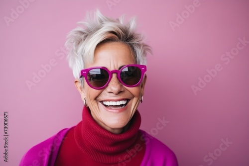 Portrait of a happy senior woman wearing sunglasses against a pink background