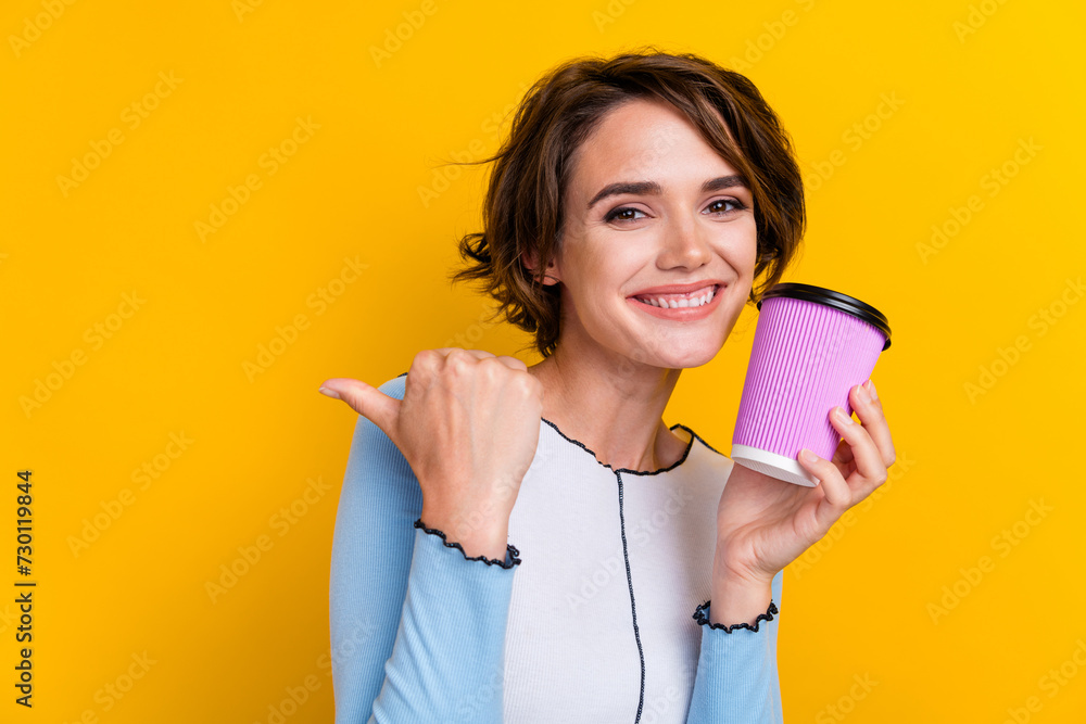 Portrait of cheerful lovely lady toothy smile hold coffee cup direct finger empty space isolated on yellow color background