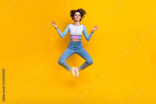 Full length portrait of carefree pretty nice person jump flying meditate isolated on yellow color background © deagreez