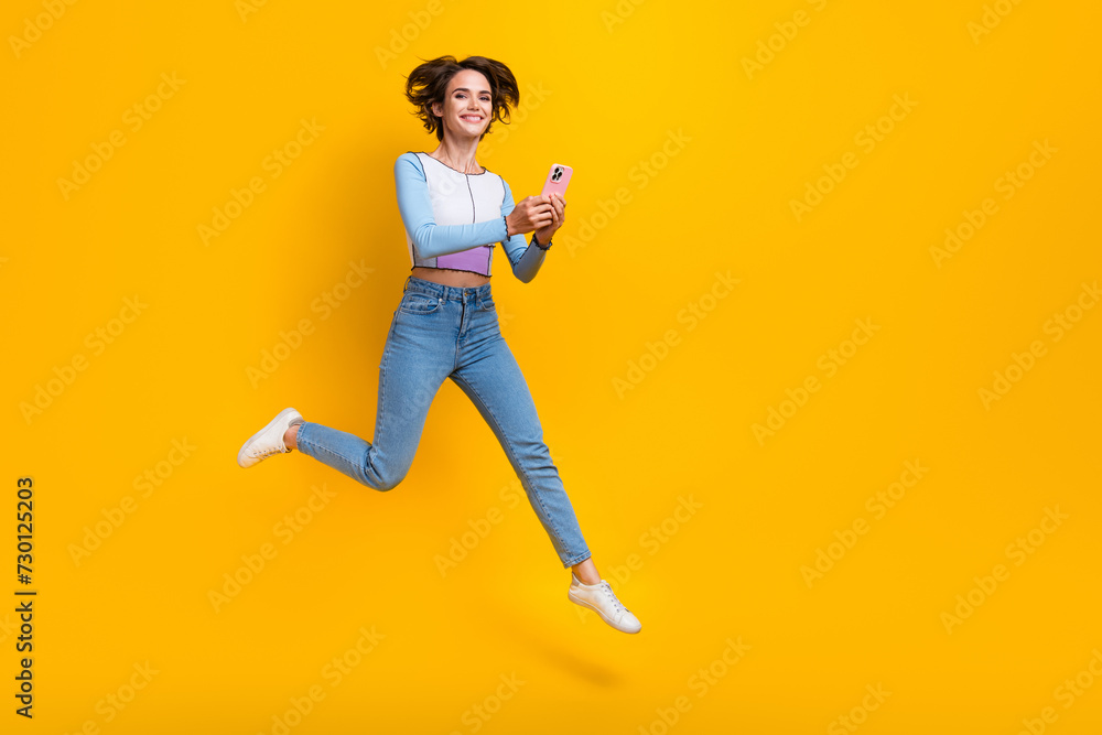 Full length portrait of carefree nice person jump hold use smart phone empty space isolated on yellow color background