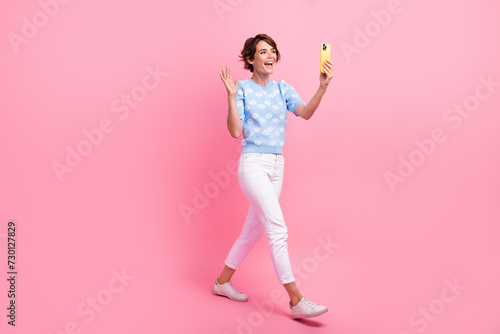 Full body profile portrait of excited pretty lady walk hold smart phone video call arm palm waving hi isolated on pink color background © deagreez