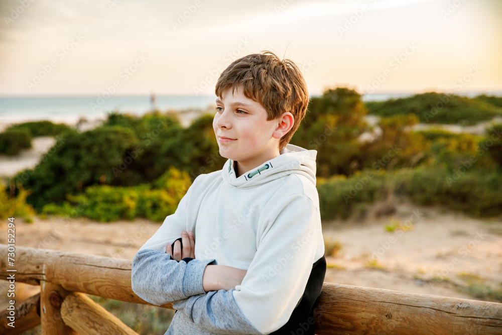 Happy cheerful teenager standing on beach at sunset. happy preteen boy smiling at the camera. Kid on family vacation at the sea.