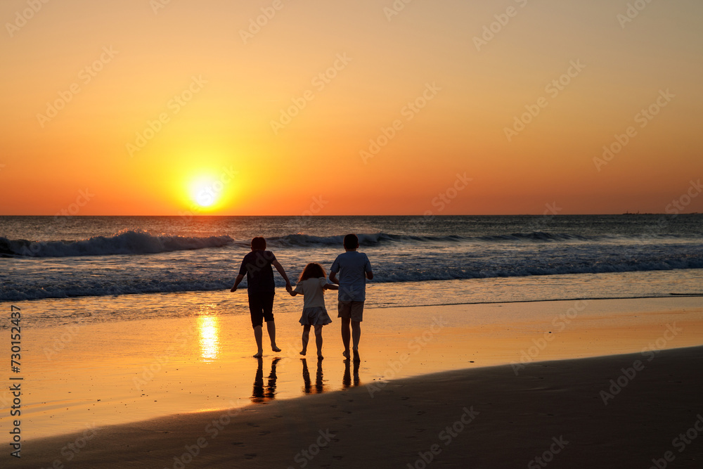 Three kids silhouettes running and jumping on beach at sunset. happy family, two school boys and one little preschool girl. Siblings having fun together. Bonding and family vacation.