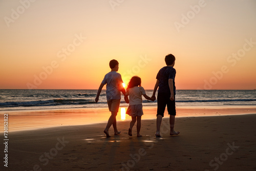 Three kids silhouettes running and jumping on beach at sunset. happy family, two school boys and one little preschool girl. Siblings having fun together. Bonding and family vacation.