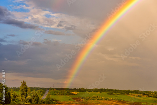 A colorful rainbow after the rain over the fields and the highway in the distance.