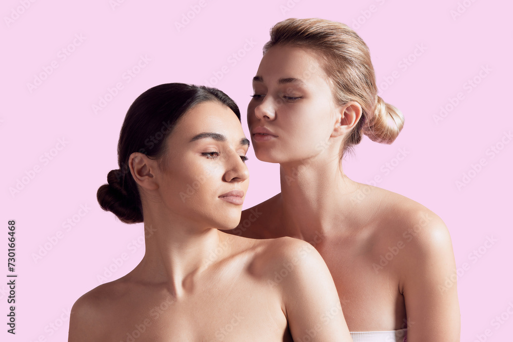 Tender and elegant young girls, brunette and blonde models with well-kept skin posing against pink studio background. Concept of natural beauty, cosmetology and cosmetics, skincare Tender and elegant young girls, brunette and blonde models with well-kept skin posing against pink studio background. Concept of natural beauty, cosmetology and cosmetics, skincare