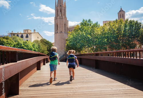 Kids tourists with backpacks run on bridge in Girona town photo