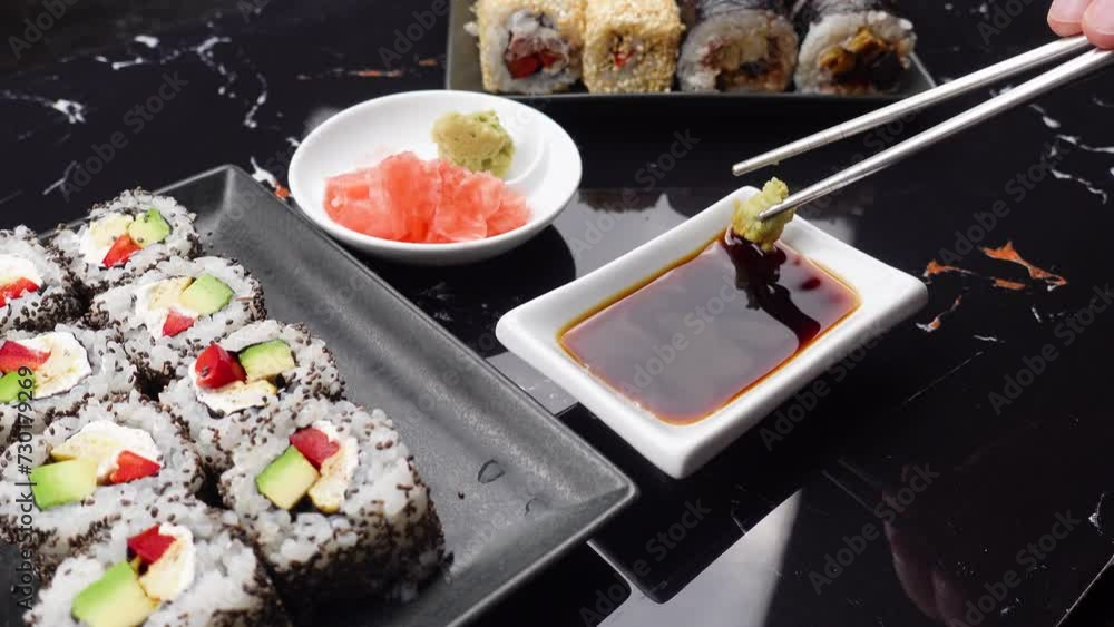 Close up of hands with chopsticks eating japanese food. Traditional asian rolls. Maki sushi with vegetables and tuna. Wasabi and Soy Sauce in bowl. Close up of hands with chopsticks eating japanese food. Traditional asian rolls. Maki sushi with vegetables and tuna. Wasabi and Soy Sauce in bowl.