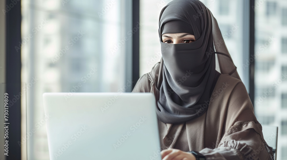 A Muslim woman in a niqab uses a laptop, blending modernity and tradition. Arabian businesswoman in niqab or black garment (abaya) works on a laptop A Muslim woman in a niqab uses a laptop, blending modernity and tradition. Arabian businesswoman in niqab or black garment (abaya) works on a laptop