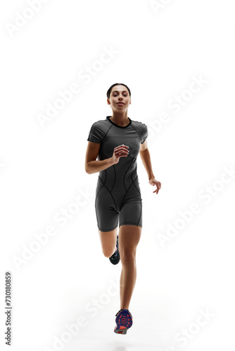 Full-length image of young girl, runner athlete in gray sportswear in motion, running, training against white studio background. Concept of sport, active and healthy lifestyle, sportswear, competition