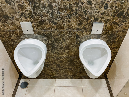Brown bathroom with two urinals and plumbing fixtures made of composite material in a rectangular shape.