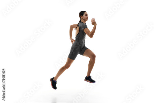 Side view dynamic image of athletic young woman in grey sportswear, runner in motion, training against white studio background. Concept of sport, active and healthy lifestyle, sportswear, competition