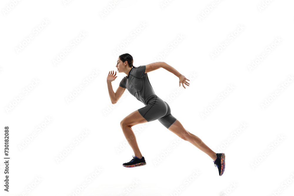 Side view dynamic image of completive young woman in grey sportswear, runner in motion, training over white studio background. Concept of sport, active and healthy lifestyle, sportswear, competition