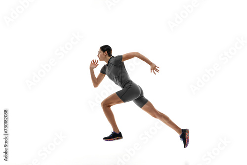 Side view dynamic image of completive young woman in grey sportswear, runner in motion, training over white studio background. Concept of sport, active and healthy lifestyle, sportswear, competition