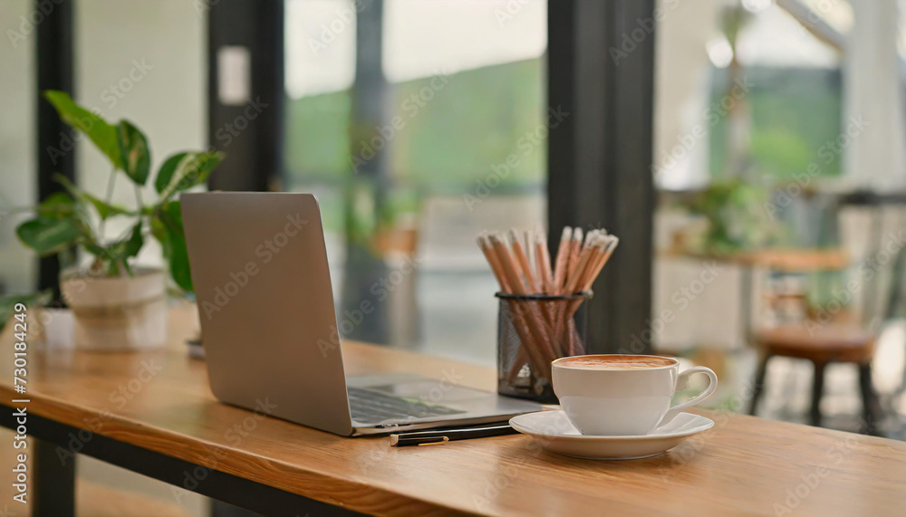 Hand holding laptop with blank screen on wooden table in cafe . Mockup image