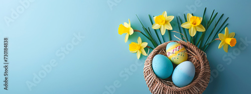 colorful easter eggs in a basket with daffodils on pastel blue background, banner with copyspace, top view photo