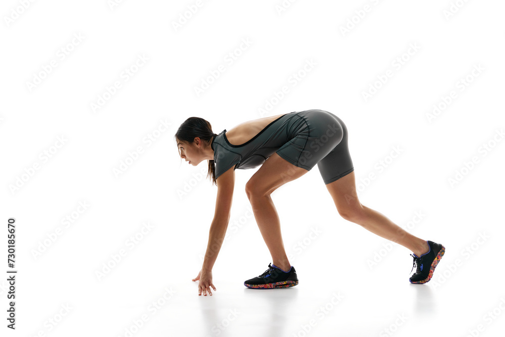 Ready, steady, go. Female runner athlete in grey jumpsuit, sportswear training against white background. Concept of sport, active and healthy lifestyle, sportswear, competition