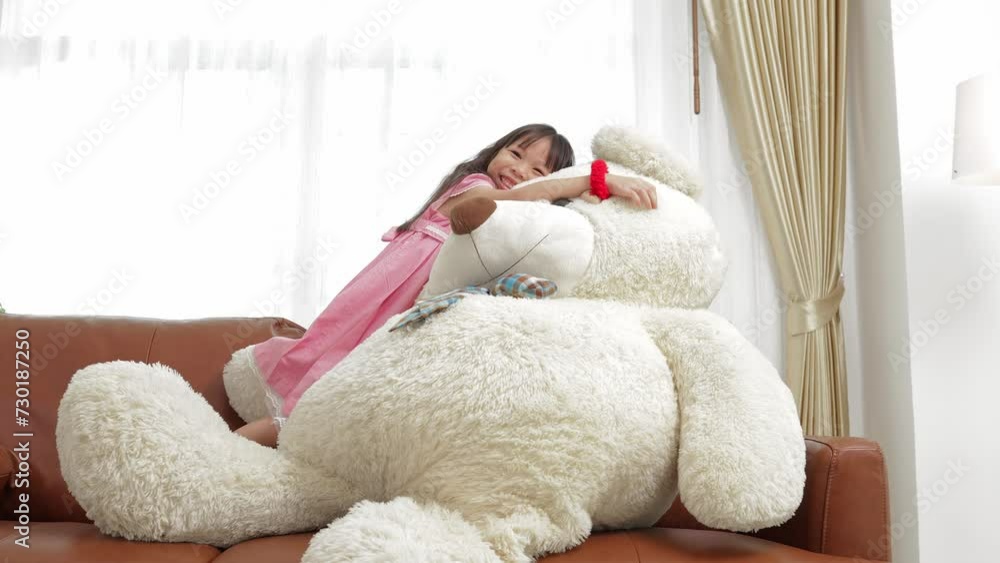 Cute little Asian girl hugs a big white teddy bear on the sofa in the living room. She is happy with the gift. best friend bear Cute little Asian girl hugs a big white teddy bear on the sofa in the living room. She is happy with the gift. best friend bear
